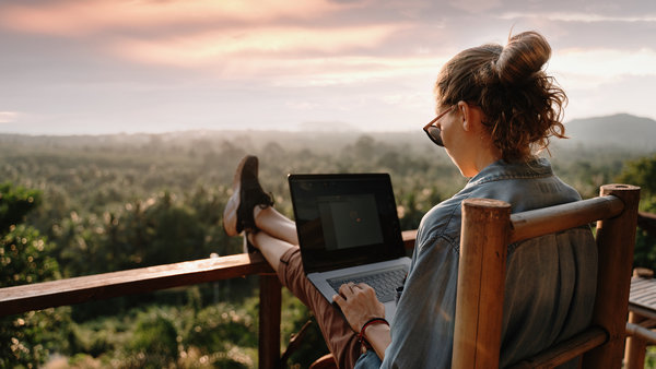 Eine Frau arbeitet in der Natur an einem Laptop. Christliche und technische Icons tauchen auf.